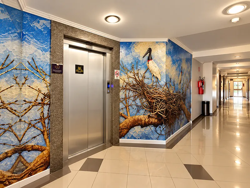 Corredor dos elevadores com painel artístico de um tuiuiú do Pantanal