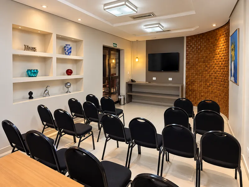 Sala de reunião com cadeiras, TV de tela plana e iluminação indireta